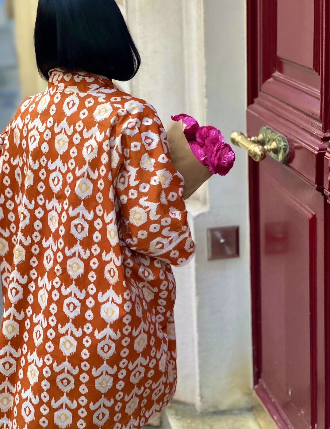 Kimono Le Madja en batik orange porté devant une porte rouge